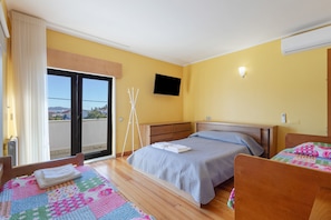 Una habitación de hotel con cama, una silla, televisor y balcón.