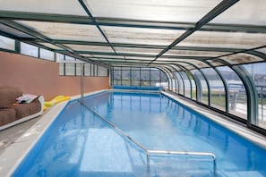 Una piscina interior con techo de cristal, un área de descanso con sofá y vistas al exterior.