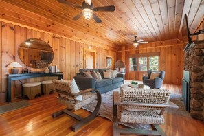L’intérieur chaleureux d’un chalet, avec un décor en bois, une cheminée en pierre et une grande fenêtre.