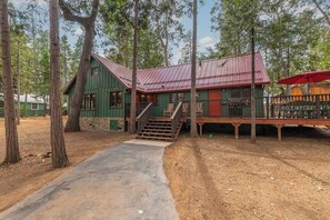 Une cabane rustique avec un toit en métal, une terrasse en bois et un escalier menant à un porche.