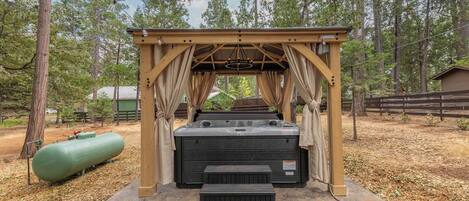 Un jacuzzi bajo una pérgola de madera en un área boscosa.
