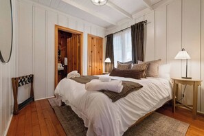 Une chambre avec deux lits, une armoire en bois, une table de chevet avec une lampe et une chaise.