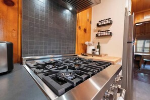 Une cuisine équipée d’une cuisinière à gaz en acier inoxydable, d’un dosseret de crédence en carreaux noirs, de meubles de rangement en bois et d’un porte-épices fixé au mur.