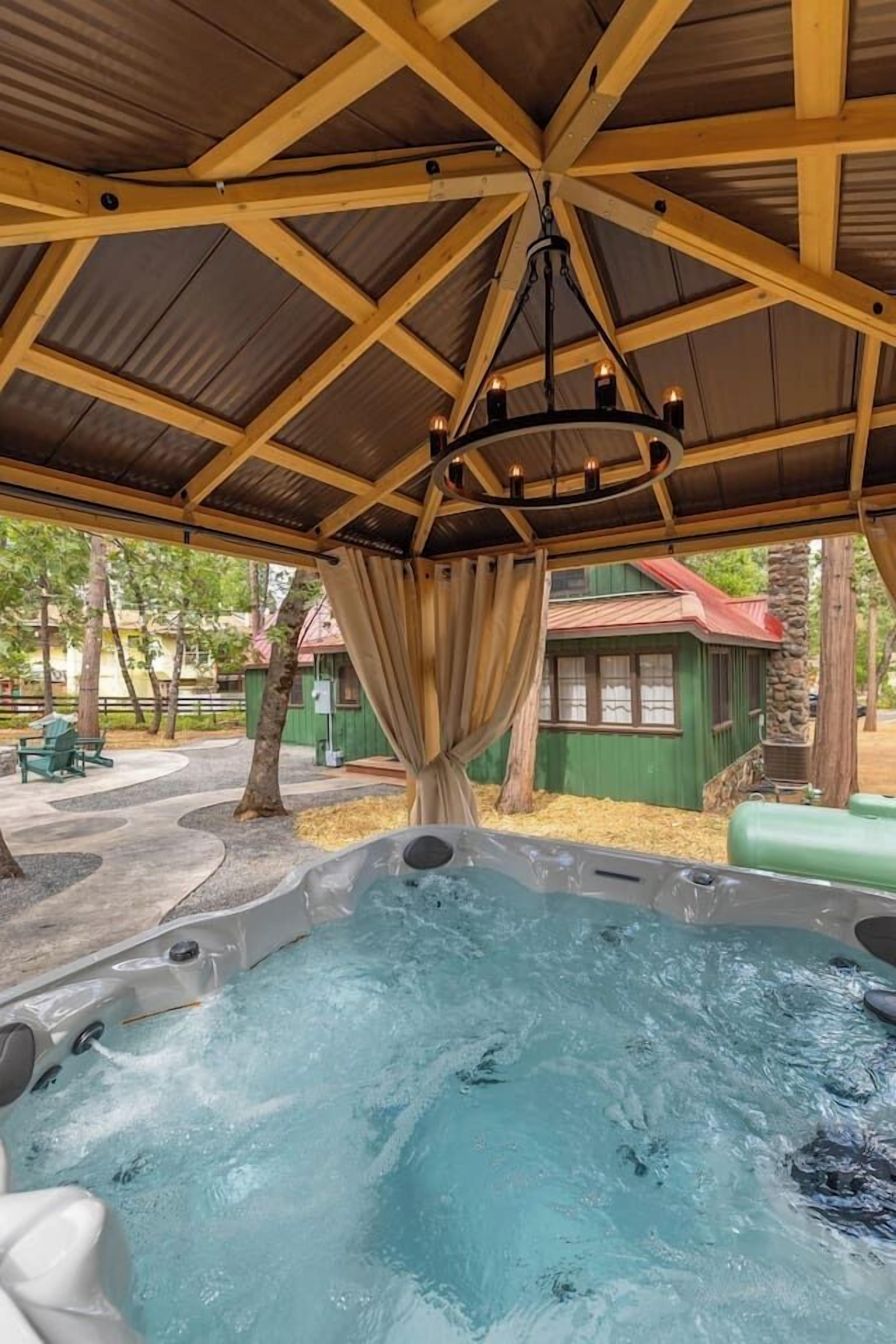 A hot tub under a wooden pergola with a view of a green building and trees.