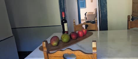 A dining area with a wooden table and chairs, a bottle of wine, and a plate of apples.
