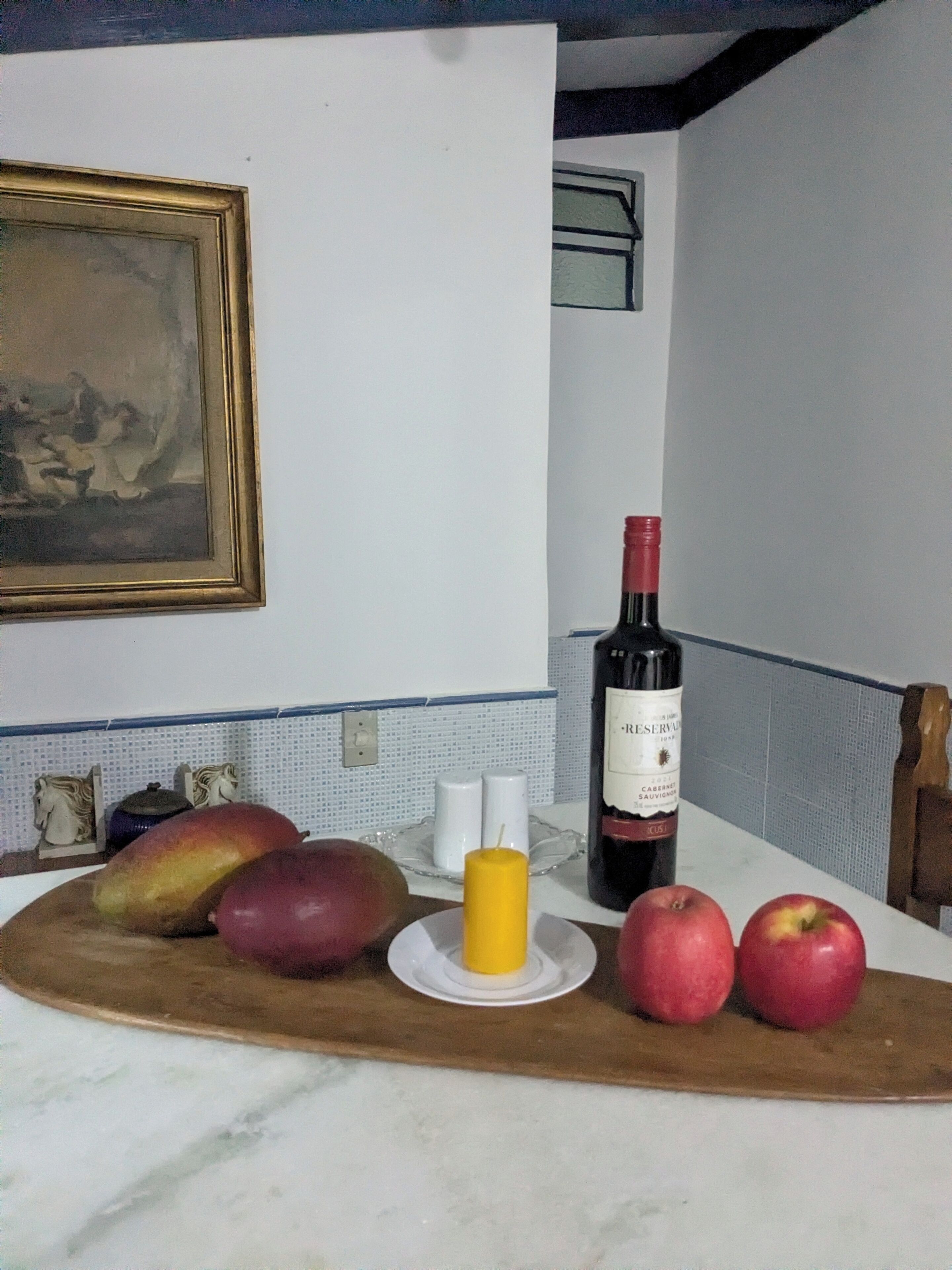 A kitchen counter with a wine bottle, apples, a candle, and decorative items.