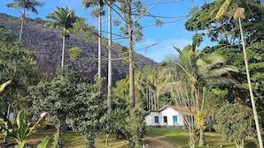 A white building with a red roof, surrounded by tropical vegetation and a mountain in the background.