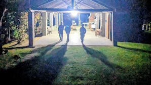 A covered outdoor area with a roof structure, a pathway leading to it, and a few people walking towards it.