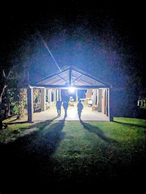 A covered outdoor area with a roof structure, a pathway leading to it, and a few people walking towards it.