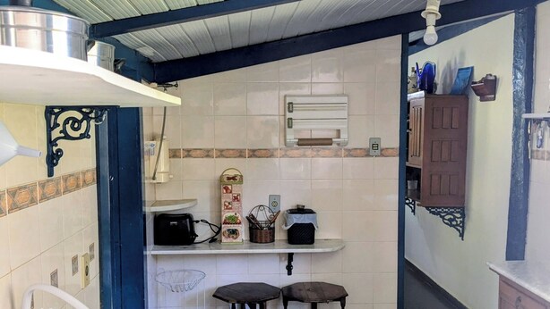 A compact kitchen with a sink, a stove, and a small countertop. There are two stools and a cabinet.