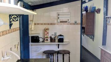 A compact kitchen with a sink, a stove, and a small countertop. There are two stools and a cabinet.
