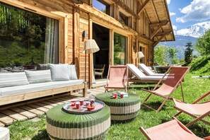 Eine Holzhütte mit einer Couch und Lounge-Sesseln, einem Esstisch mit Tassen sowie Blick auf Berge.