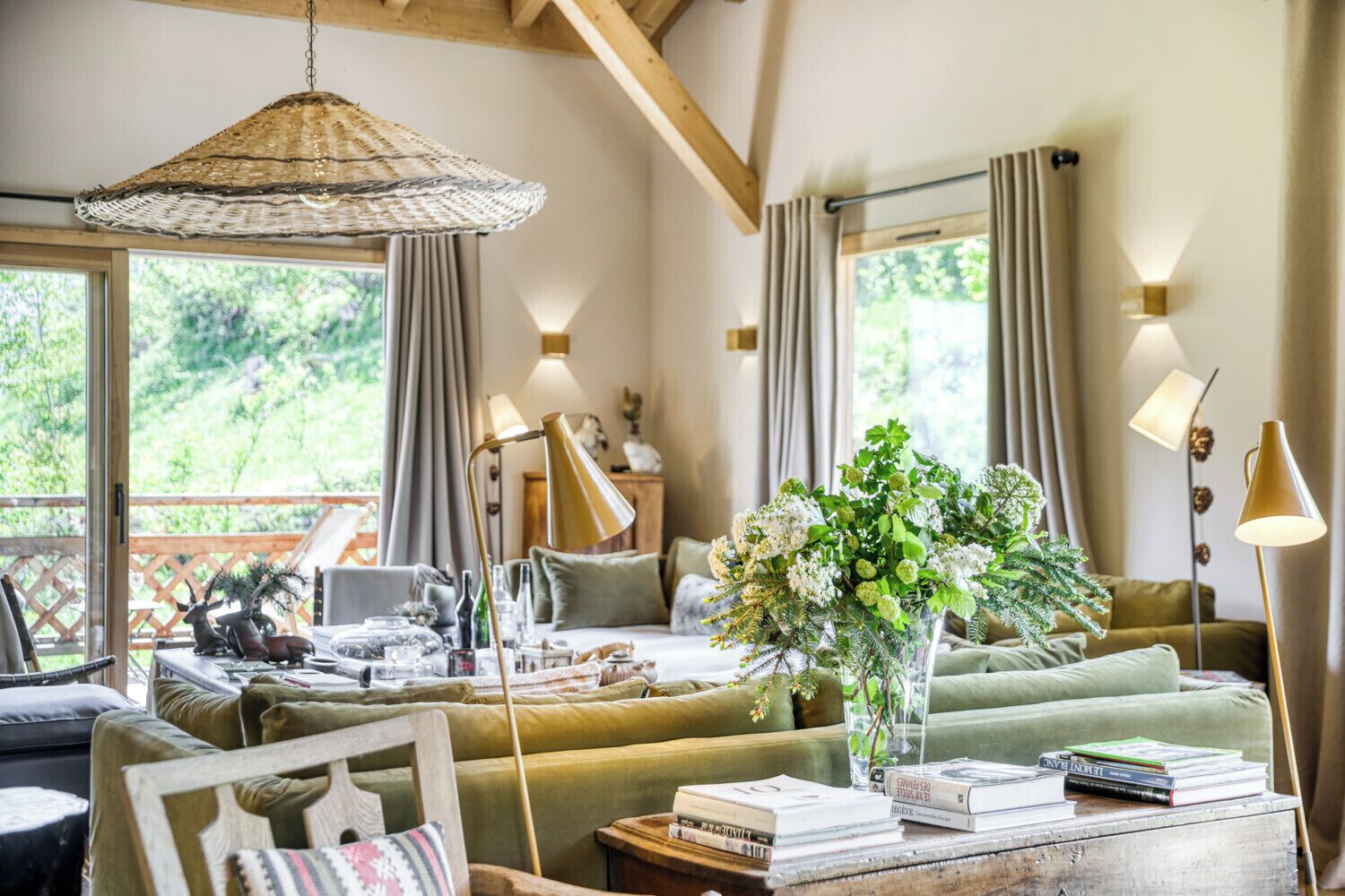 A cozy living room with a sofa, a coffee table with books, a hanging light fixture, and a view of greenery outside.