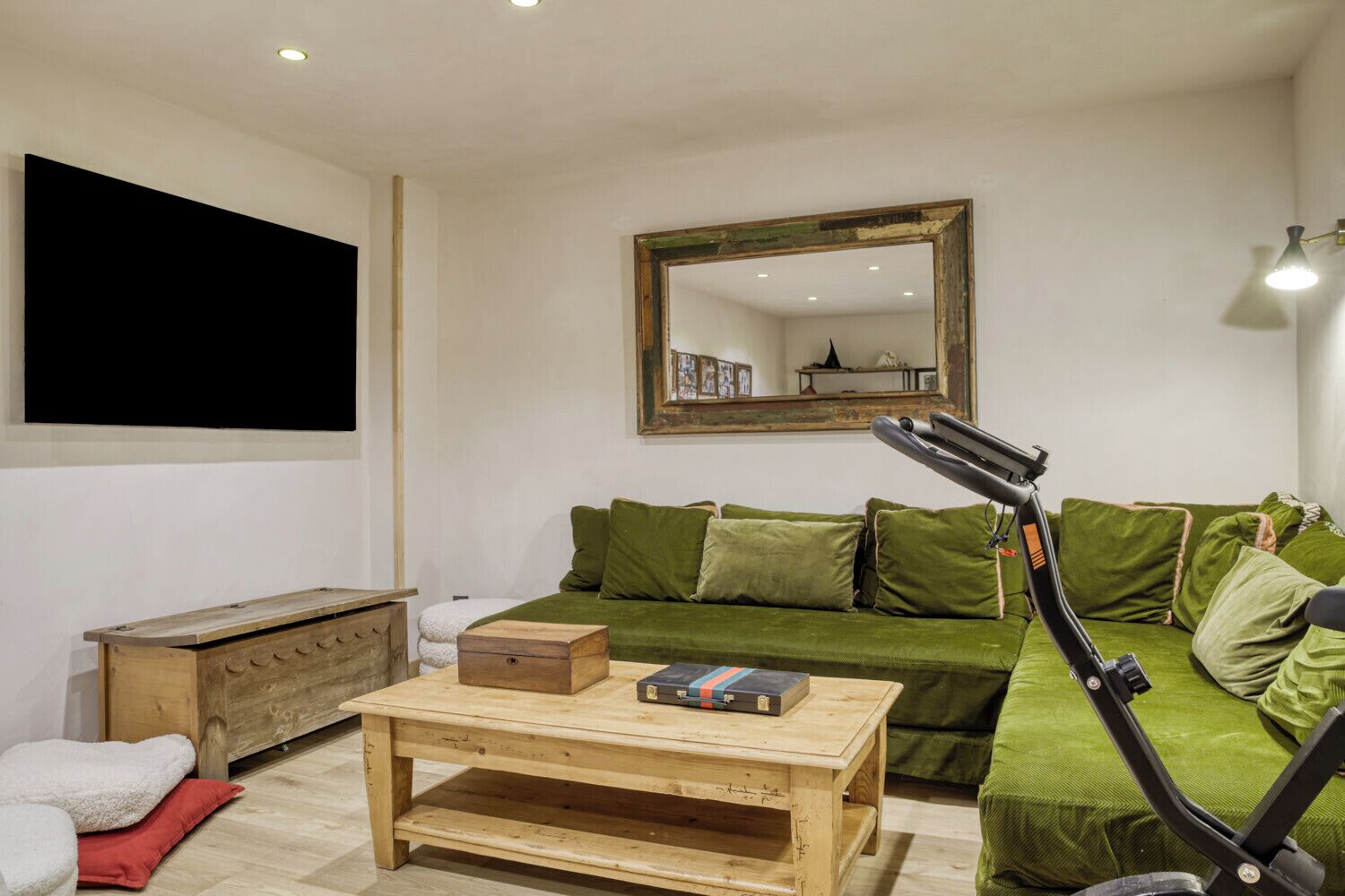 Een woonkamer met een groene bank, een houten salontafel, een houten kist en een staande lamp.