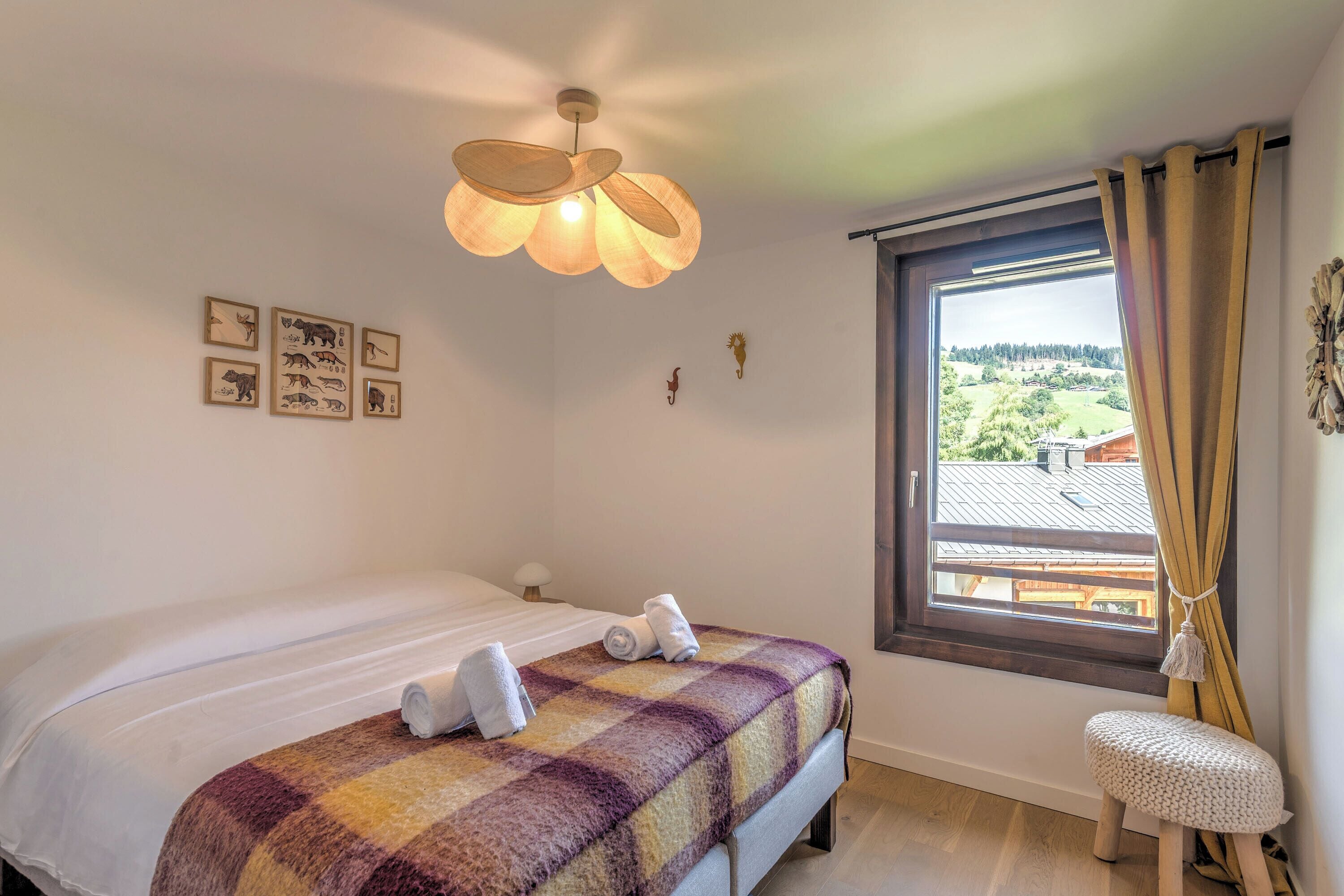 Un dormitorio con cama, ventana con cortinas, lámpara de pared y ilustraciones enmarcadas de animales.