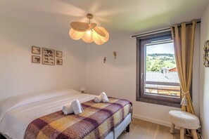 Quarto com cama, janela com cortinas, luminária fixada na parede e ilustrações emolduradas de animais.