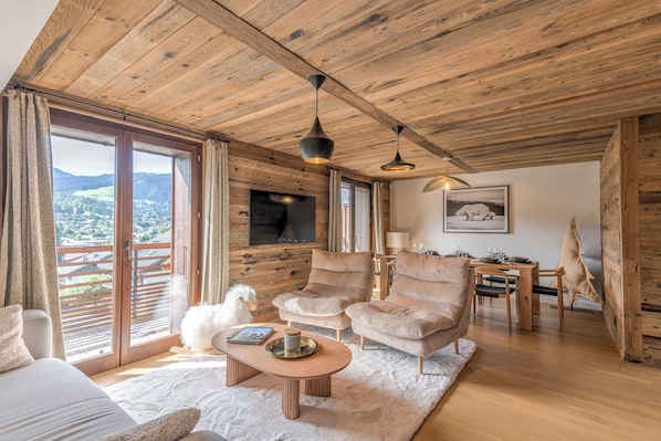 Un salon chaleureux avec un plafond en bois, de grandes fenêtres, une cheminée et un coin repas offrant une vue agréable.