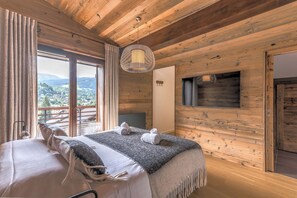 Une chambre dans une cabane en bois, avec un lit, un luminaire suspendu et une vue sur un paysage montagneux.