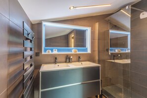 Une salle de bain moderne avec deux lavabos, un grand miroir et un espace douche.