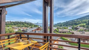 En balkon med et gult bord og stole, der ud til et landsbylandskab med traditionelle huse og bjerge i baggrunden.