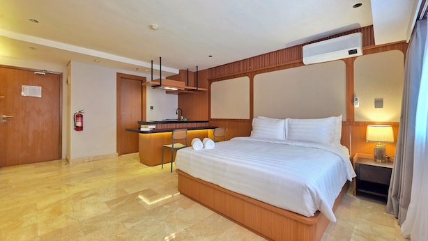 Habitación de hotel con una cama grande, un escritorio pequeño, una silla, un minibar y la puerta del baño.