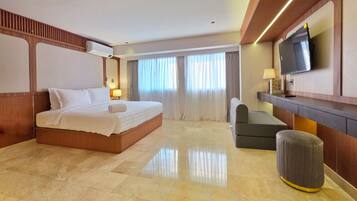 Quarto de hotel com uma cama grande, televisão, escrivaninha e uma cadeira.