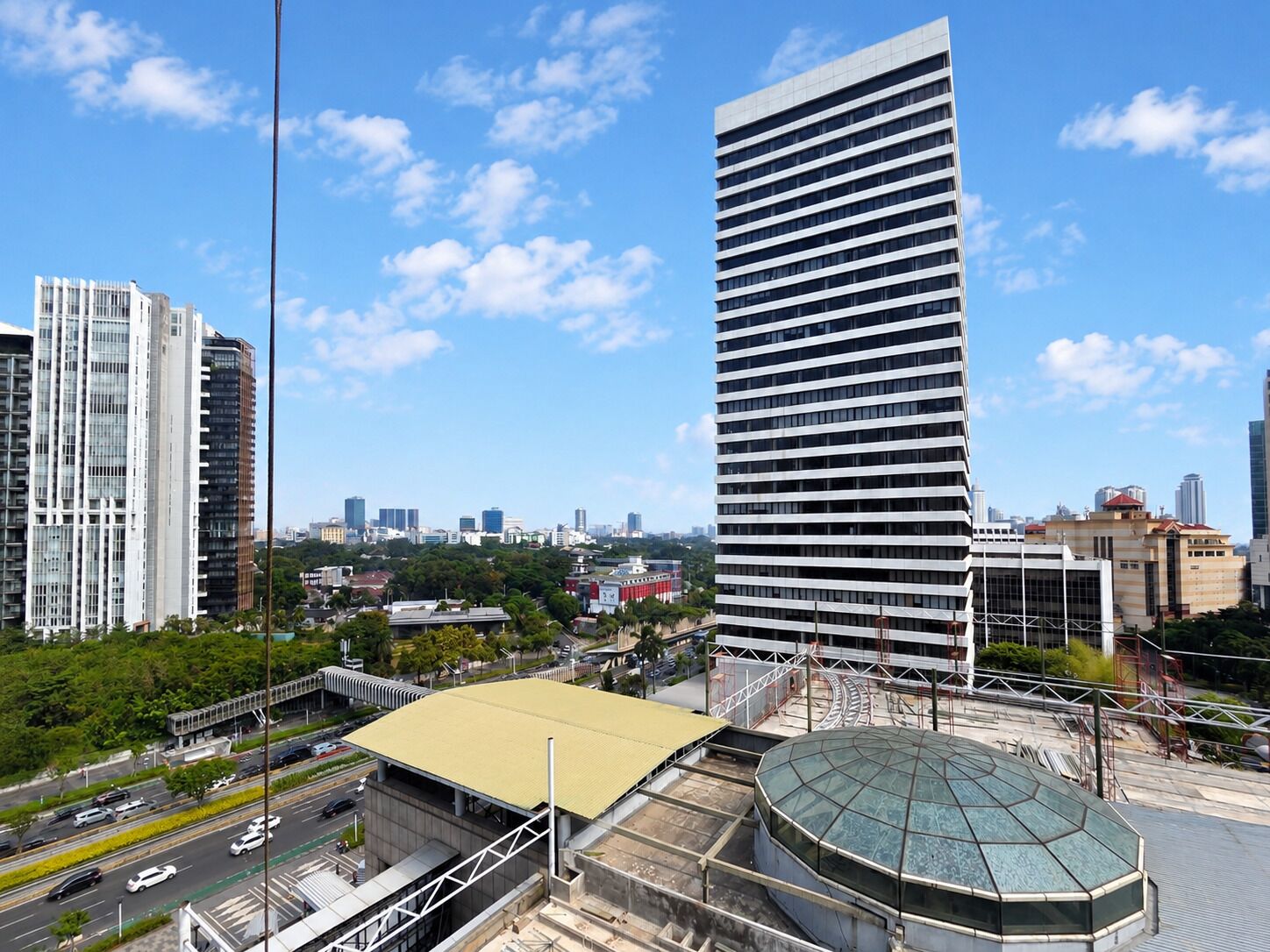 A cityscape with modern high-rise buildings, a large circular structure, and a road with vehicles.