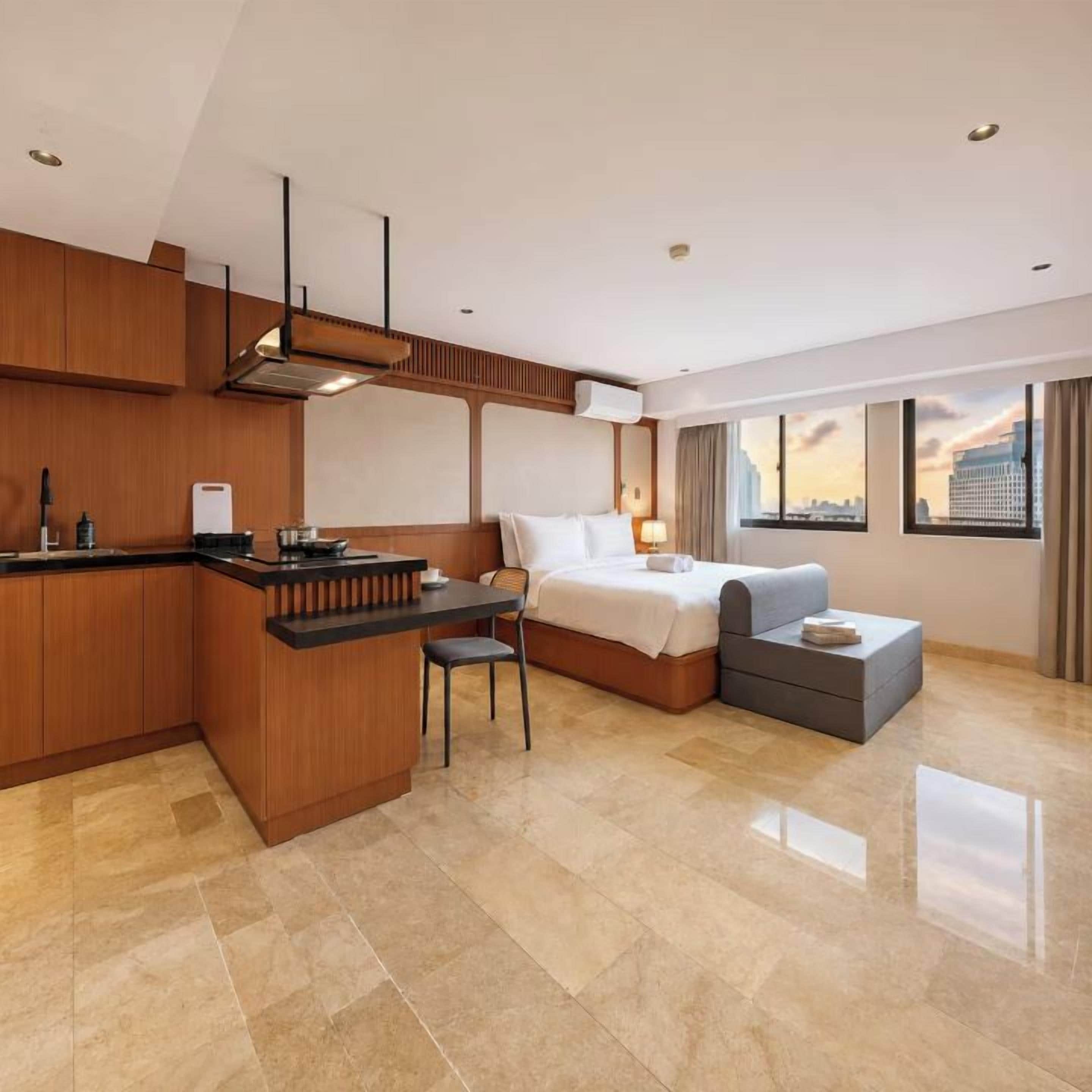 Habitación de hotel moderna con kitchenette, cama, zona de estar y un amplio ventanal con vistas a la ciudad.