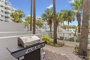 An outdoor grill area with a view of a pool and palm trees. - Destin West ~ Sandpiper L07 ~ Walk Out Lanai with Private Grill ~ Lazy River (Fort Walton Beach)