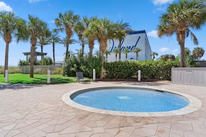 A swimming pool with a hexagonal tile pattern, surrounded by palm trees and a building with a blue and white facade. - Destin West ~ Sandpiper L07 ~ Walk Out Lanai with Private Grill ~ Lazy River (Fort Walton Beach)