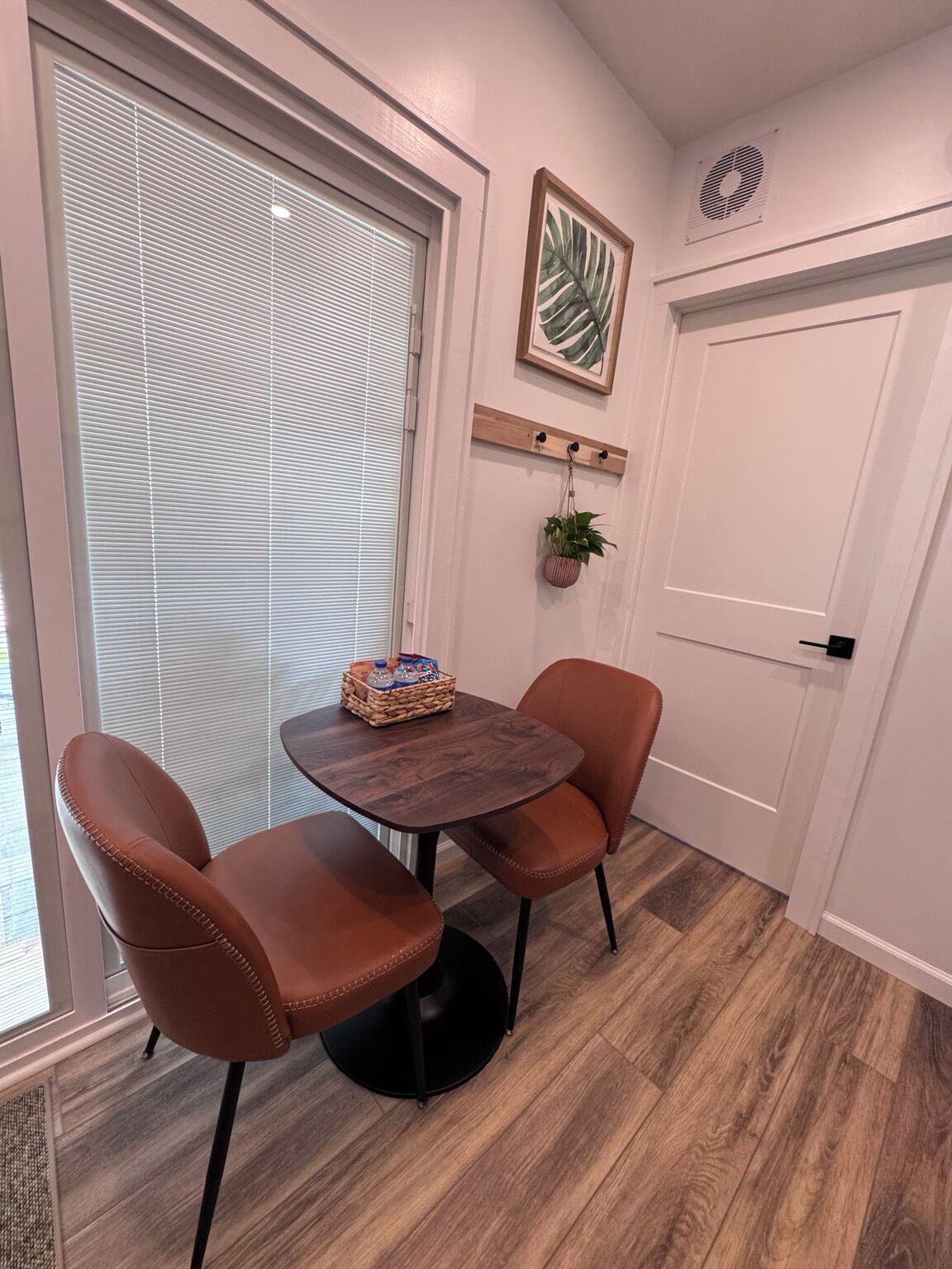 A room with a round wooden table, two brown leather chairs, a small plant, and a framed picture on the wall.