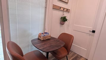 A room with a round wooden table, two brown leather chairs, a small plant, and a framed picture on the wall.