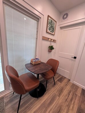 Een kamer met een ronde houten tafel, twee bruine lederen stoelen, een klein plantje en een ingelijst beeld aan de muur.