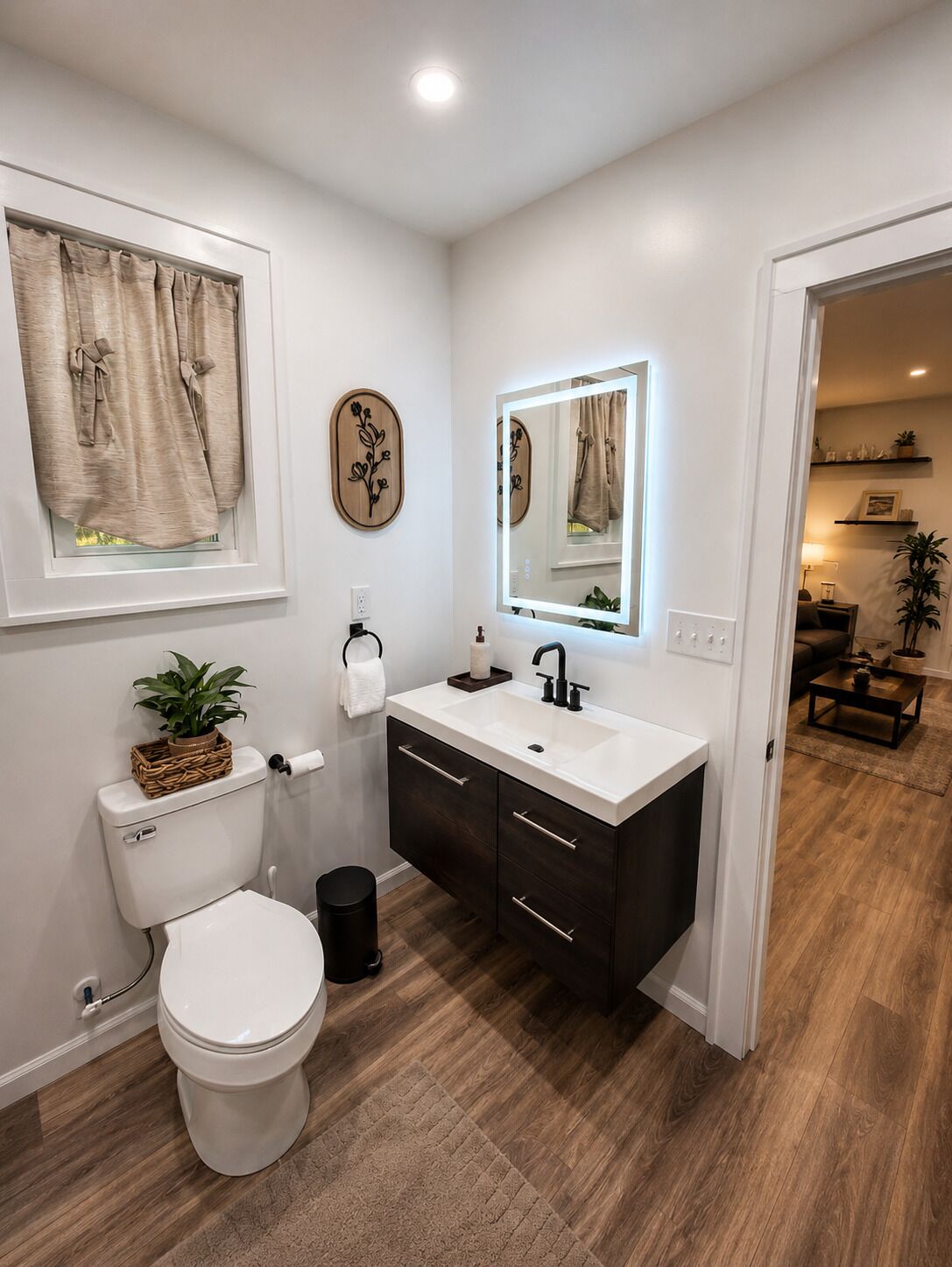 A modern bathroom with a white toilet, dark wooden cabinets, a white sink, and a mirror with a light above it.