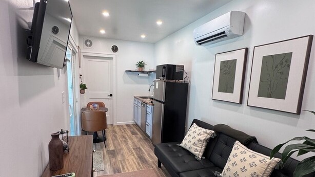 Un espacio habitable compacto con sofá, televisor, zona de cocina y mesa de comedor.