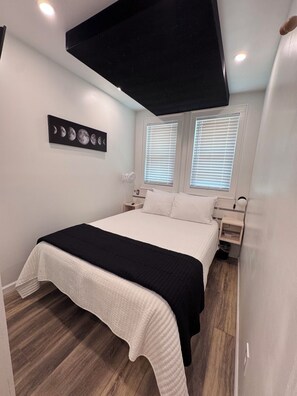 A bedroom with a bed, bedside tables, a wall-mounted artwork, and a ceiling light fixture.