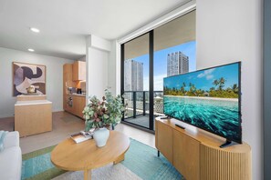 A modern living room with a large flat-screen TV, a wooden coffee table, a sofa, and a kitchen area with wooden cabinets. - The Crosby 2BR Luxury City Views Balcony (Miami)