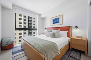 A modern hotel room with a large bed, a nightstand, a bedside table, a framed picture on the wall, and a view of the building outside. - The Crosby 2BR Luxury City Views Balcony (Miami)
