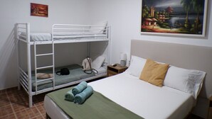 Ein Zimmer mit einem Etagenbett, einem Bett mit grüner Decke, einem Nachttisch mit Lampe und einem Bild an der Wand.