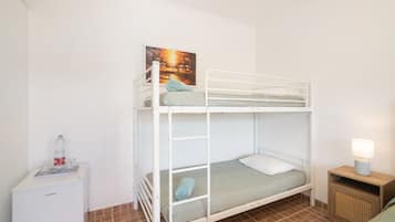 Una cama litera con un almohadón y una toalla enrollada, una mesita de noche con una lámpara y un cuadro en la pared.