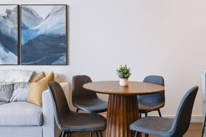 Ein modernes Wohnzimmer mit einem grauen Sofa, einem runden Holztisch und vier grauen Stühlen. Auf dem Tisch steht eine Topfpflanze.