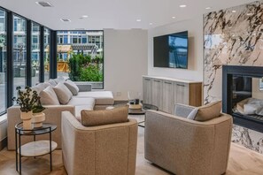 A modern living room with a sofa set, a TV mounted on the wall, and a fireplace. - The Aqua Vista | 2 Bed, Lake Views w Pool, Hot tub (Kelowna)