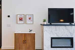 Ein modernes Wohnzimmer mit einem Flachbildfernseher, der über einem Marmor-Kamin angebracht ist, einem Holzschrank mit der Zahl '11' darauf und zwei gerahmten Bildern an der Wand.