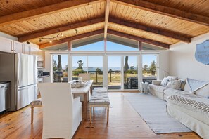 A spacious living area with a high ceiling, a kitchen with a refrigerator, and a large sliding glass door leading to an outdoor patio.