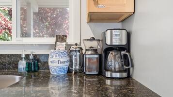 Un plan de travail de cuisine avec une machine à café, une dosette de café torréfié à la française, un récipient à farine et un distributeur d’eau.