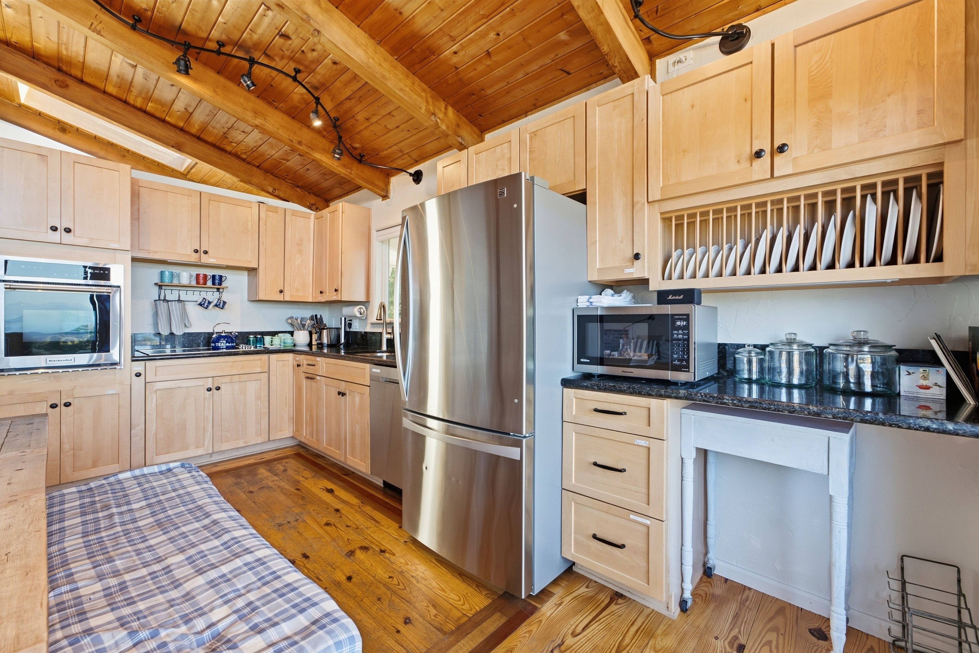 Een moderne keuken met houten kastjes, roestvrijstalen apparatuur en een eethoek met een geruit tafelkleed.
