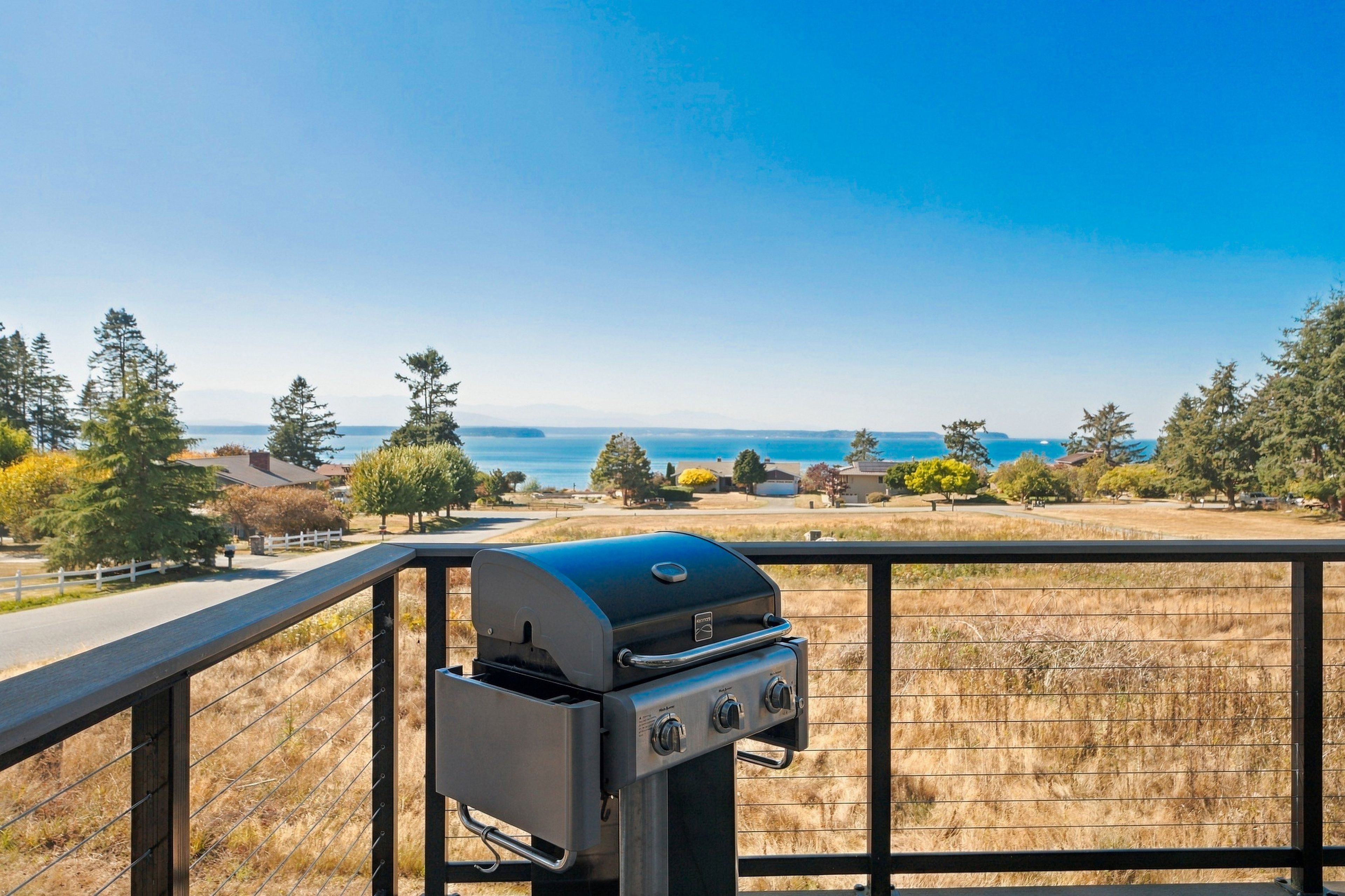 A barbecue grill on a balcony overlooking a residential area with houses and trees.