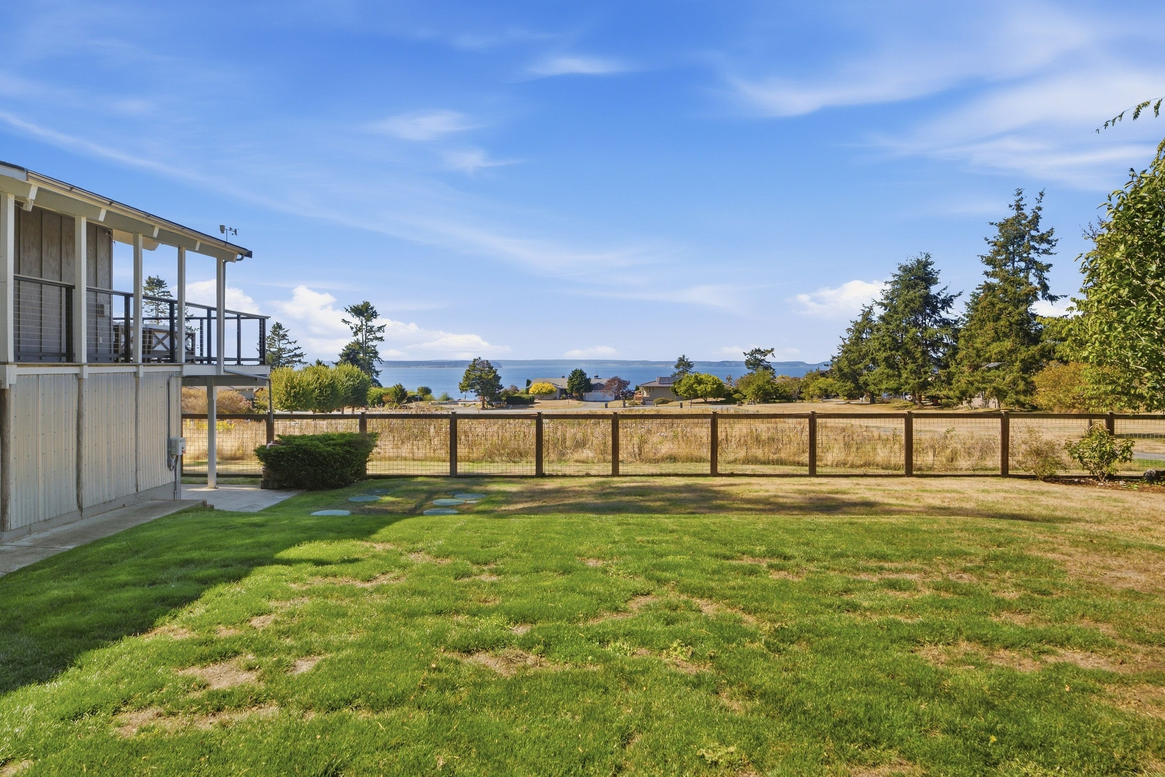 A residential property with a fenced yard, a covered porch, and a view of the sea.