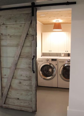 Ett tvättrum med två tvättmaskiner och en dörr av trä.