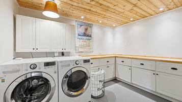 A laundry room with two front-loading washing machines, a drying rack, and a wooden ceiling.